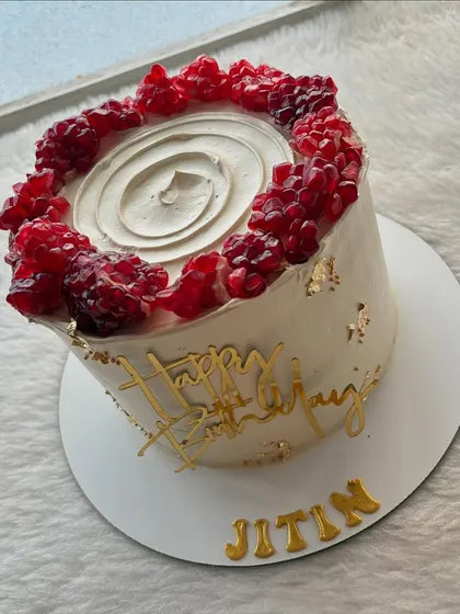 A beautiful cake topped with fresh pomegranate jewels. The vibrant red of the fruit looks stunning against the white cream and gold accents.