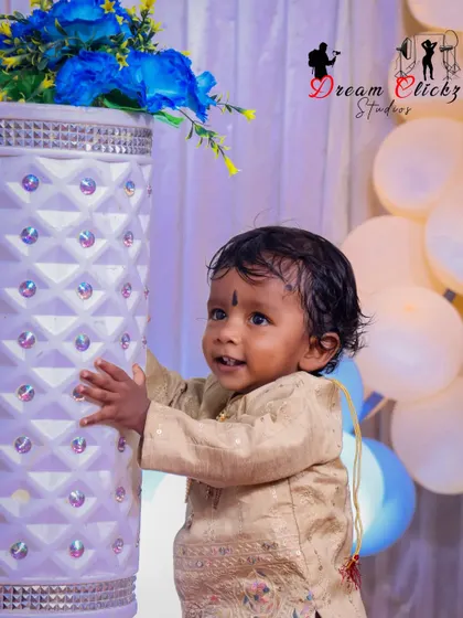 A candid moment from a first birthday shoot. This little boy is captured looking up with a curious expression, with party balloons and decorations creating a festive atmosphere.