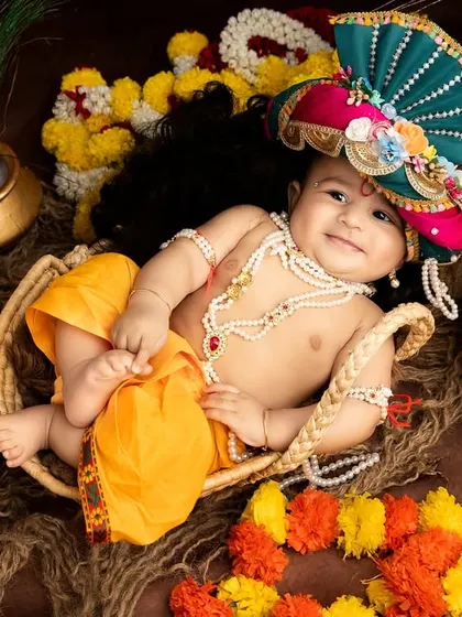 A joyful baby Krishna lying in a basket, surrounded by colorful flowers and pots. His smile truly lights up the photo.
