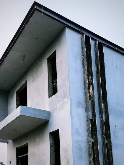 A modern house with its concrete structure and plastering nearly complete. The sharp lines and cantilevered balcony are key features of the design.