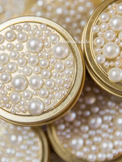 A touch of glamour for your home. This golden tin jar candle is topped with a lid adorned with a cascade of pearls, making it a beautiful decorative object even when not lit.