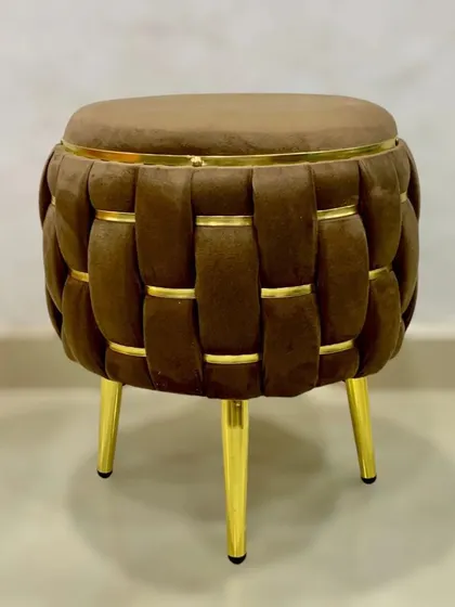 A stylish and versatile puffy stool, upholstered in rich brown velvet with a woven pattern and accented with golden patti and legs.