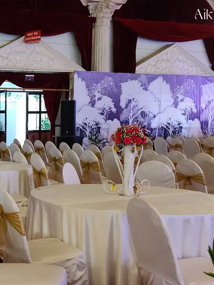 Elegant guest seating with white covers and gold bows. The backdrop features a subtle tree silhouette design, adding a touch of nature-inspired art to the indoor venue.