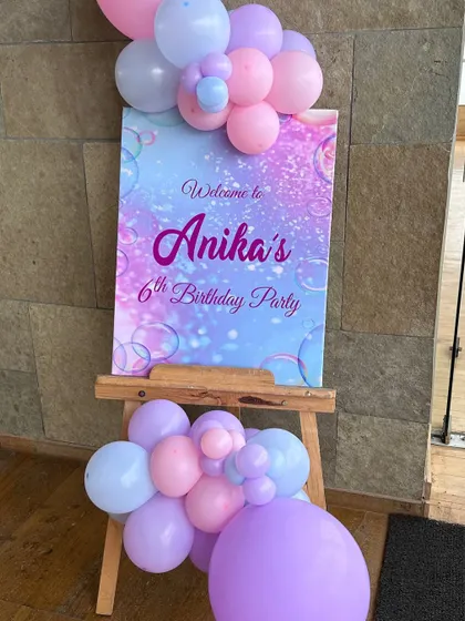A custom welcome sign for Anika's 6th birthday party. The easel stand is decorated with a small balloon arrangement, setting the tone for the mermaid theme right from the entrance.