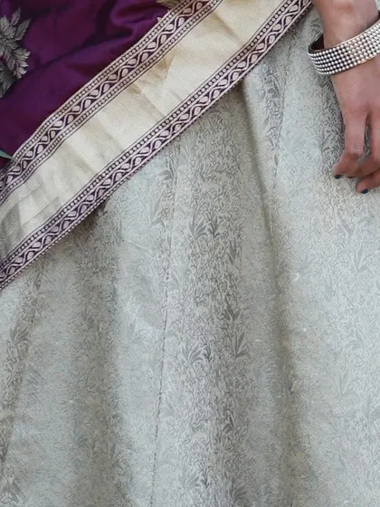 A detail of the cream-colored brocade skirt and the contrasting purple border, showing the rich texture of the fabric.