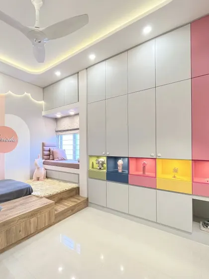 A full view of the kids' room, showing the platform bed with integrated storage and a whimsical, backlit cloud-shaped false ceiling detail. The wardrobe features pops of color in its open niches.