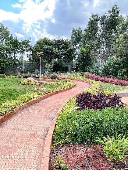 A winding pathway at 'The Sanctuary' meanders through a newly planted garden, with a large natural rock formation serving as a sculptural element in the landscape.
