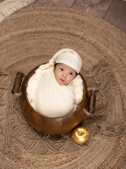 An alert newborn in a wooden bowl, looking right at the camera. The single golden apple prop adds a touch of whimsy to this simple and engaging portrait.