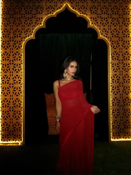 A dramatic shot of Nysa framed by a beautifully lit archway, making the red of the saree stand out against the night.