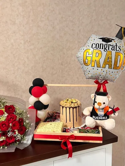 A perfect gift for a new graduate. This tray hamper includes a custom cake, a personalized teddy bear, a bouquet of red roses, and a "Congrats Grad" balloon.