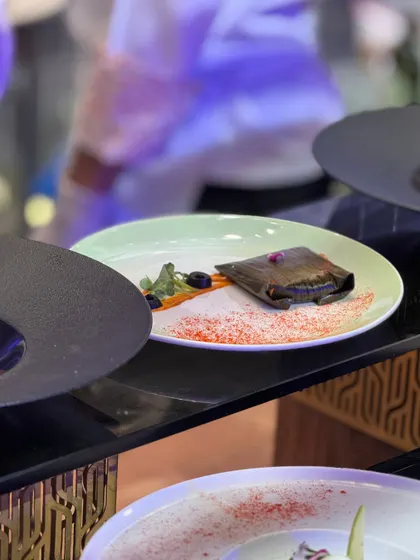 A dish wrapped in a banana leaf, presented on a modern plate with a colourful spice dusting. This fusion of traditional cooking methods and contemporary plating is a hallmark of our culinary style.