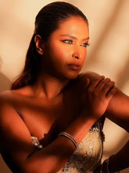 A close-up under dramatic lighting. This highlights the beautiful bronze tones on the skin and the sharp, clean lines of the eye makeup.