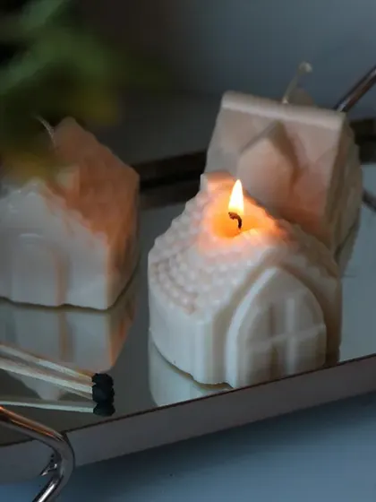 A lit house-shaped candle, casting a warm and inviting glow. A perfect addition to your Christmas decor.