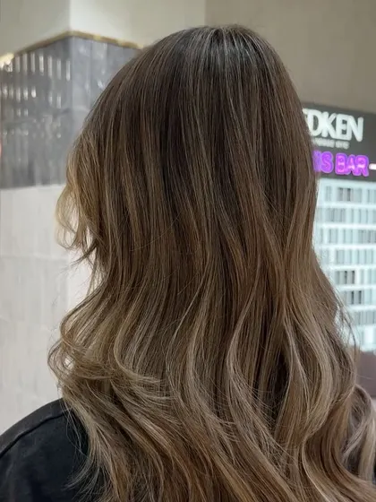 This close-up highlights the cool, ashy tones and the dimension created by the balayage technique, with the Redken gloss bar in the background.