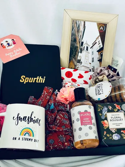 A personalized Rakhi hamper featuring a "Sunshine" mug, a custom-named notebook for 'Spurthi', and a variety of pampering goodies.