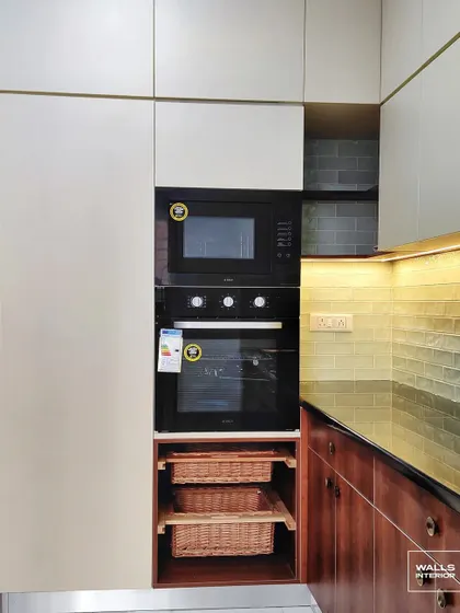 A tall kitchen unit designed for appliances, featuring a built-in oven and microwave. Below, pull-out wicker baskets provide breathable storage for vegetables.