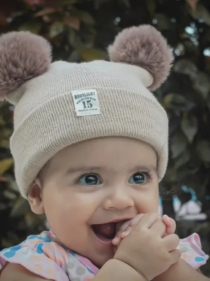 A baby's smile can make a house shine without the sun. This close-up portrait captures the pure, heart-melting happiness of a baby in a cute pom-pom hat.