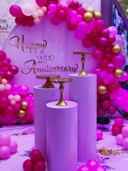 A vibrant 25th anniversary celebration with a round backdrop and a balloon arch in shades of hot pink and gold.