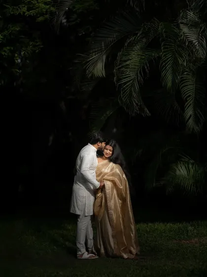 A low-light portrait in a garden, creating a soft and romantic mood. The focus is entirely on the couple's connection, with the dark greenery providing a beautiful, intimate frame.
