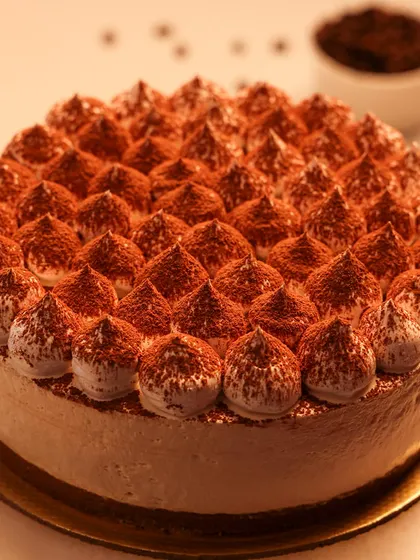 We present a taste of Italy with our classic Tiramisu cake. Featuring layers of coffee-soaked ladyfingers and creamy mascarpone, this cake is finished with piped cream and a generous dusting of cocoa powder for an authentic and elegant dessert experience.