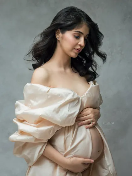 A close-up detail of the silk gown, focusing on the texture and the mother's gentle embrace of her bump. The wind in her hair adds a touch of life and movement.
