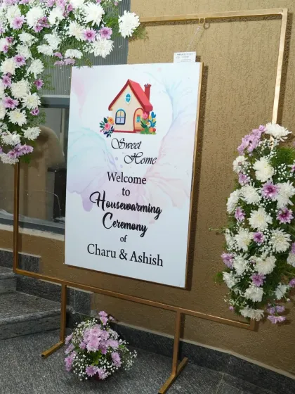 A "Sweet Home" welcome sign for Charu and Ashish's housewarming ceremony, framed with fresh flowers.