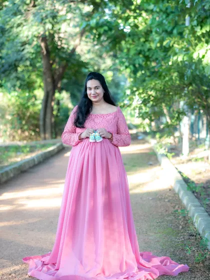 A classic outdoor portrait of a mom-to-be in a pink gown, holding a pair of tiny baby shoes.
