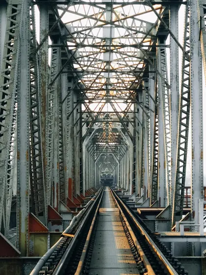 Looking down a long, symmetrical railway bridge. The repeating steel structures create a powerful leading line and a sense of infinite perspective, highlighting the beauty in industrial architecture.