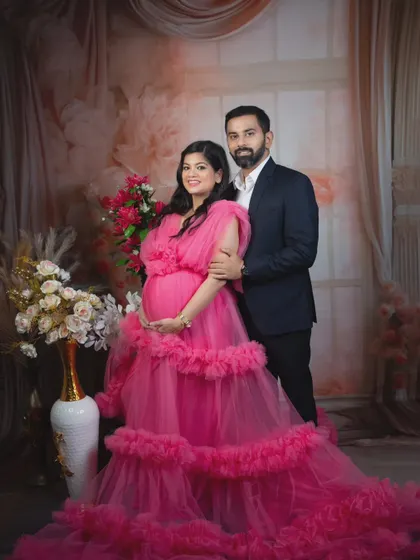 A classic portrait of an expecting couple. The mother-to-be cradles her bump in a bright pink gown.
