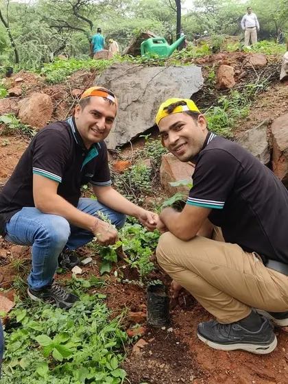 Two smiling employees from Colt Technology Services plant a sapling on the rocky terrain of Aravali Nagar Van.