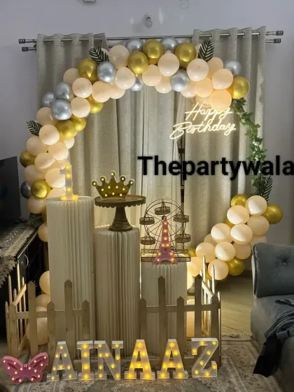 A gold, cream, and silver balloon arch in a cozy living room setting.