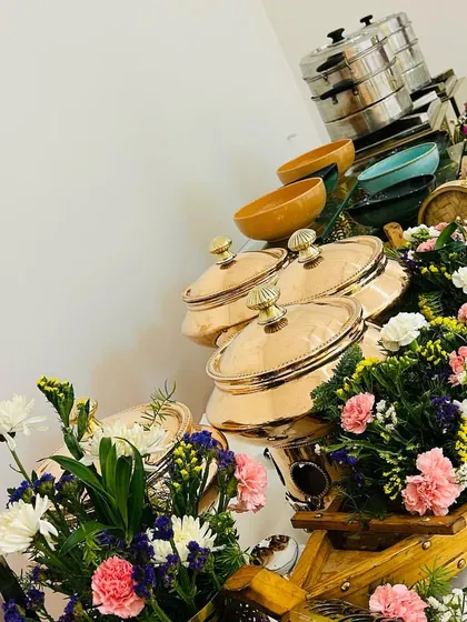 A floral-heavy buffet setup for a house party. The serving dishes are nestled within boat-shaped wooden planters filled with an assortment of fresh flowers.