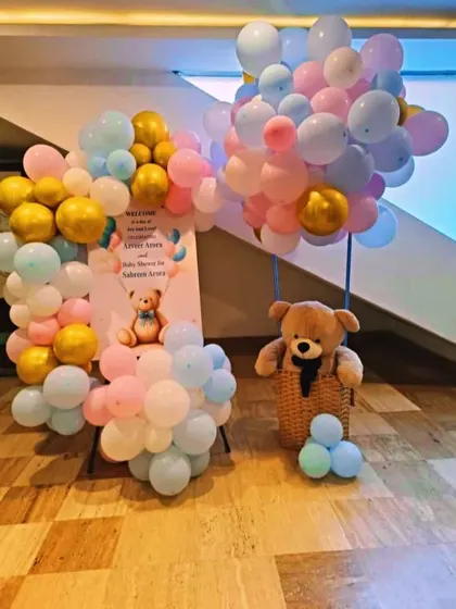 A charming welcome setup featuring a teddy bear in a hot air balloon basket made of balloons in pink, blue, and gold.