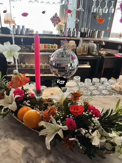 A close-up of the bar decor, featuring a stunning floral arrangement with fresh oranges, a pink candle, and a mini disco ball.