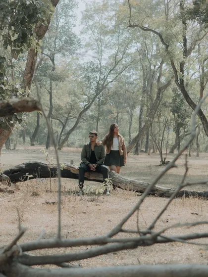 The couple takes a quiet moment on a fallen log in the middle of the forest. A serene and beautifully composed shot that speaks of peace and companionship.