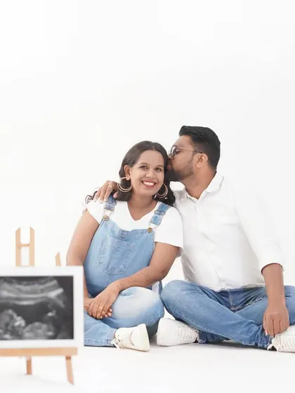 A fun and casual pregnancy announcement photo. The couple is dressed in denim, sharing a sweet moment while showcasing their baby's first picture, the sonogram.