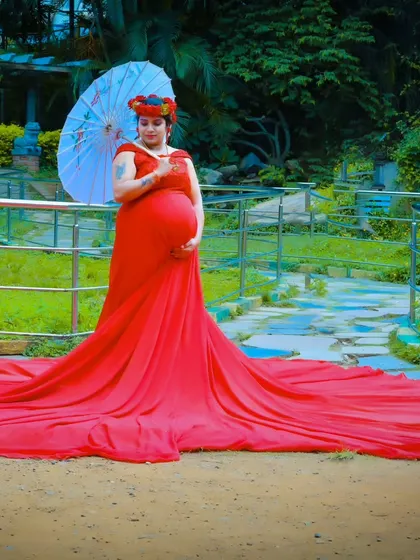 A stunning wide shot of a red maternity trail gown, spread out fully on the ground in a beautiful park setting.