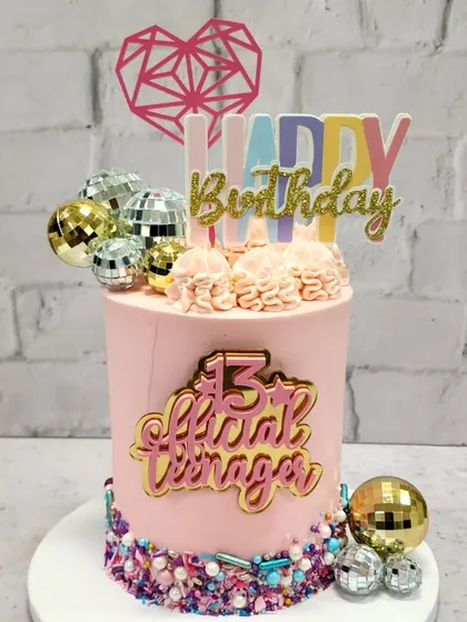 Officially a teenager! This fun and vibrant cake celebrates a 13th birthday with disco balls, sprinkles, and a cool "Official Teenager" topper.