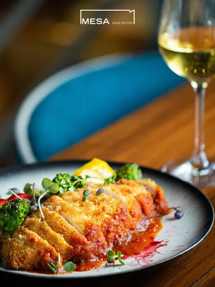 A beautifully presented breaded chicken dish from Mesa Wine Bistro, paired with a glass of white wine. This highlights the sophisticated European cuisine and wine pairings I offer.