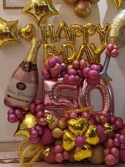 A festive balloon bouquet perfect for a 50th birthday celebration. This arrangement includes pink and gold balloons, large "50" foil numbers, and champagne bottle and glass foil balloons.