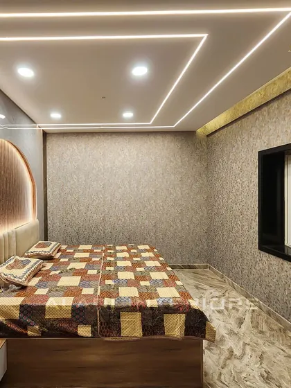 Another angle of the bedroom with the geometric ceiling lights, showing the textured wallpaper and the overall cozy ambiance created by the warm lighting.