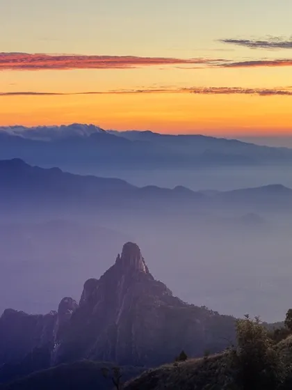 A close-up view of the unique, pointed shape of Rangaswamy Peak in the Nilgiris, shrouded in the purple and orange hues of dawn.