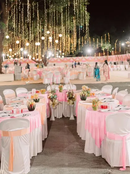 The outdoor seating arrangement under a canopy of fairy lights and paper lanterns. The pink and white color scheme for the tables created a soft, romantic ambiance for guests to dine and socialize.