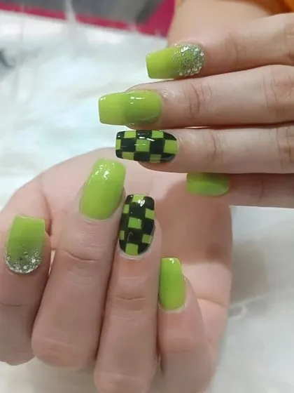 A bold lime green manicure with a black checkerboard pattern on the accent nails, finished with a touch of glitter.
