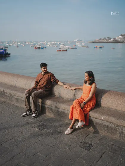 Nikit and Anusha share a quiet moment sitting on the sea wall at the Gateway of India, with the harbor and its many boats creating a classic Mumbai seascape behind them.
