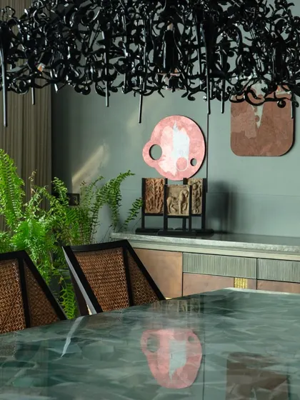 A close-up of the dining area, showing the intricate 'Hollywood' chandelier by Brand van Egmond. Its dark, sculptural form provides a dramatic contrast to the colorful art and lush greenery.