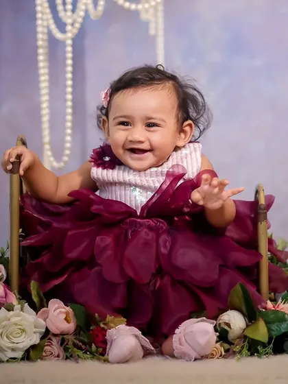 A beautiful floral swing setup. The baby is nestled in a seat surrounded by a cascade of pink and white flowers, with elegant pearls hanging from above, creating a soft and classic portrait.