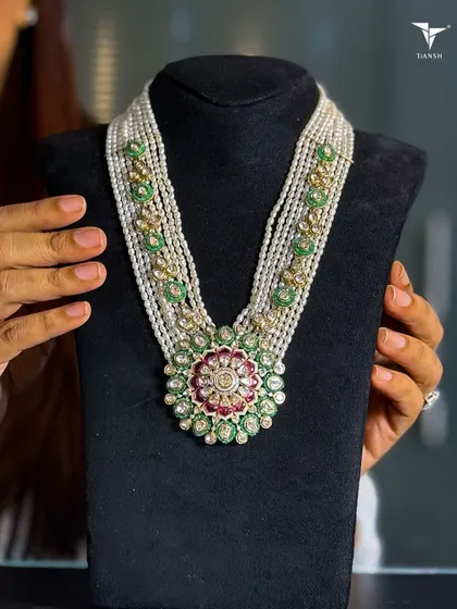 This heritage Polki necklace, held with care, showcases the intricate floral pendant and strands of pearls. It is a piece designed to be treasured for a lifetime.