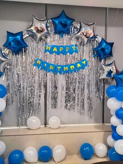 A simple yet festive backdrop using two balloon pillars and an arch of star-shaped foil balloons over a silver fringe curtain.