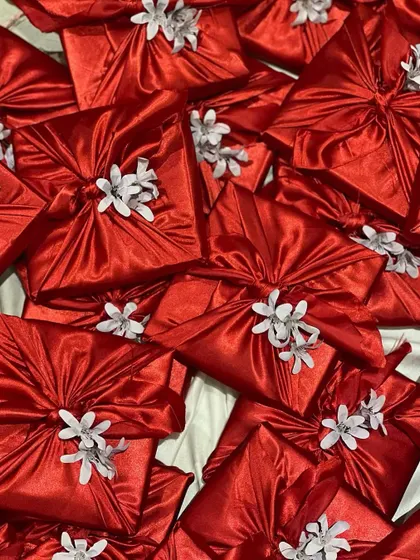 Beautifully wrapped Women's Day gifts in vibrant red furoshiki-style fabric, adorned with a delicate white flower. A sustainable and stunning way to present a gift.